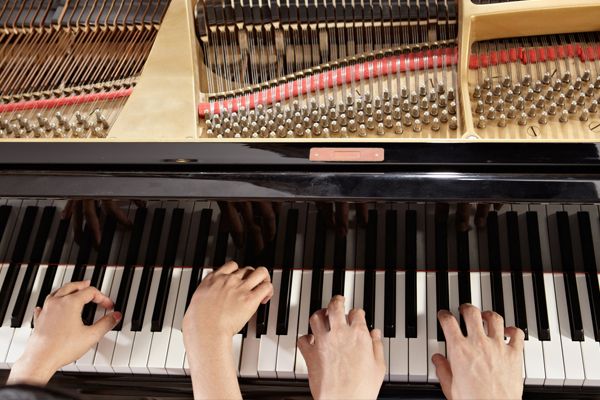 two sets of hands playing a piano.